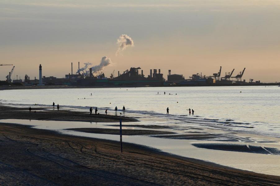 Vue sur la côte, avec des installations industrielles et de la fumée qui s'élève à l'horizon.