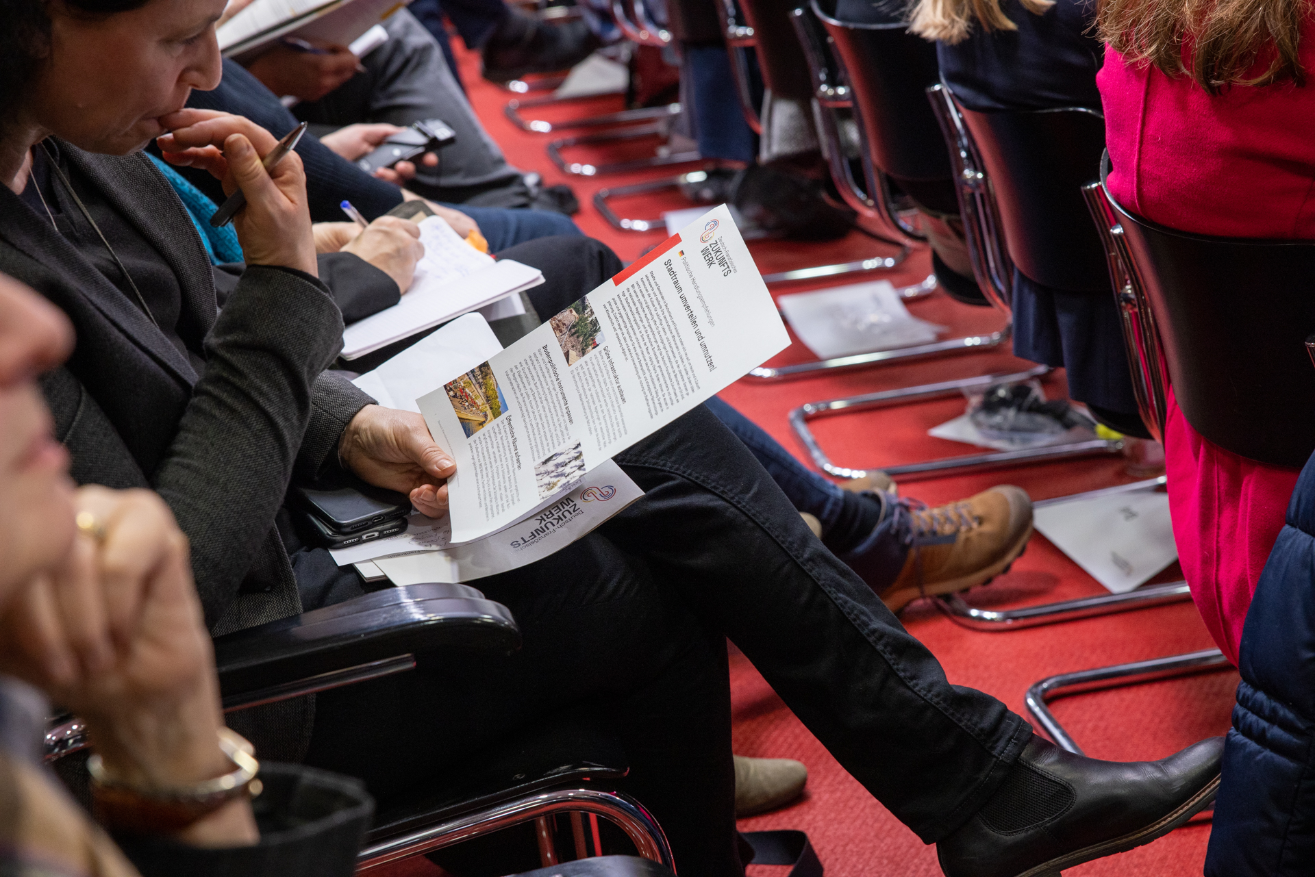 Une personne installée dans une salle de conférence tient un document dans la main.
