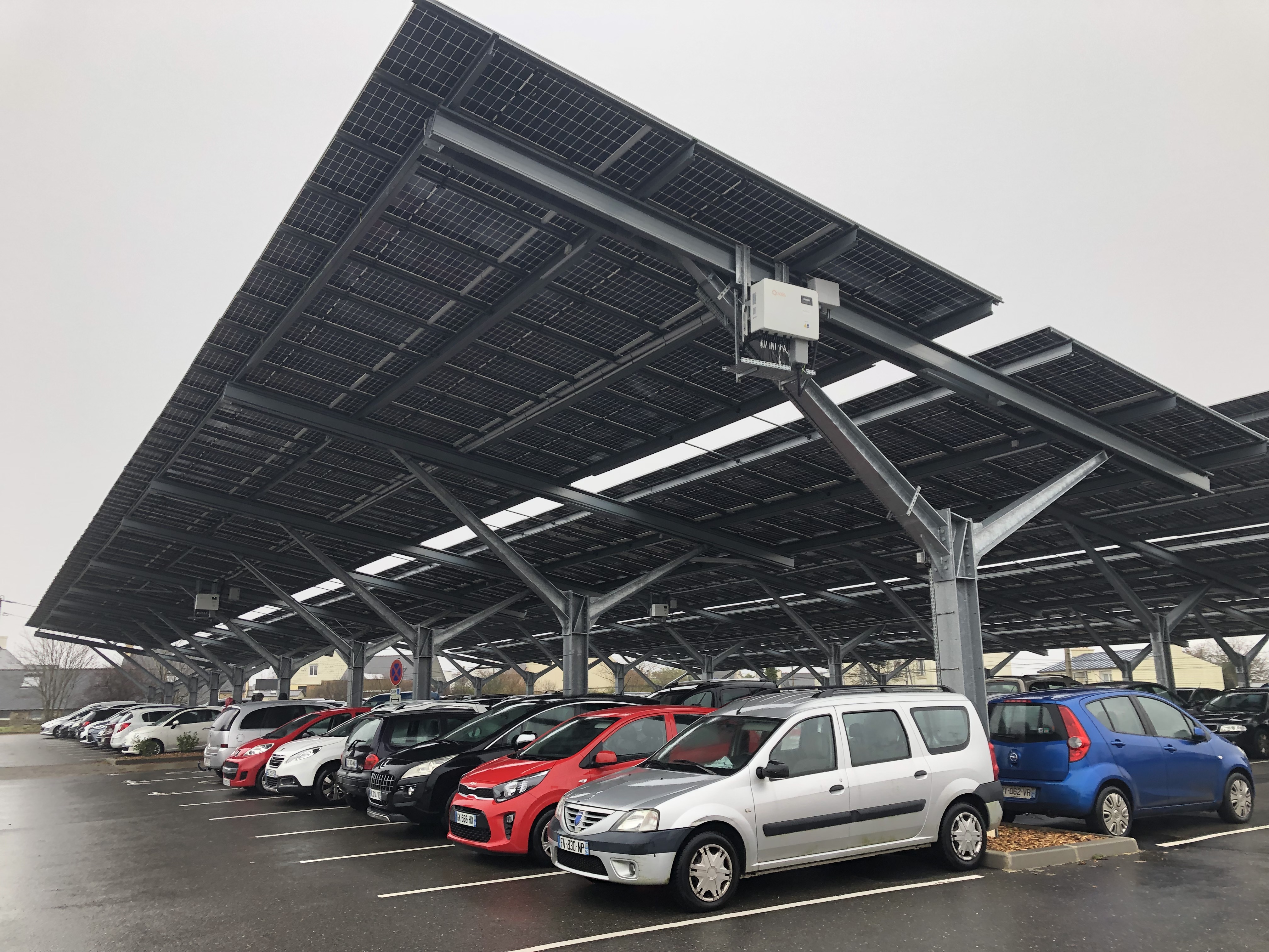 Sur un parking couvert de panneaux solaires, des voitures sont alignées sur plusieurs rangées.