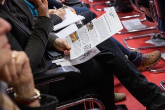 Une personne est assise dans une salle de conférence et tient un document à la main.