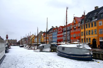 schneebedeckter Kanal mit Segelbooten, dahinter befindet sich eine bunte Häuserzeile.