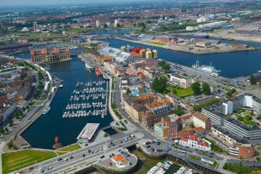 Vue aérienne : des bâtiments industriels, des habitations et des bureaux entourent le bassin portuaire de Dunkerque. 