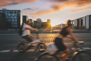 Deux personnes roulent à vélo, en fond se couche le soleil sur la ville.