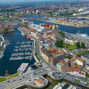 Vue aérienne : des bâtiments industriels, des habitations et des bureaux entourent le bassin portuaire de Dunkerque. 