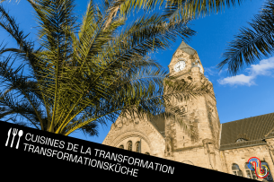 Au premier plan, un palmier vu en contre-plongée. En deuxième plan, l'horloge de la gare de Metz. En arrière-plan, le ciel bleu.