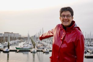 Une femme avec une veste rouge se trouve devant des voiliers. 