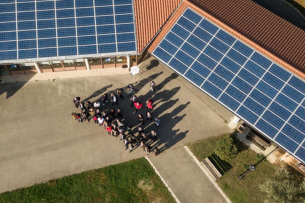 Un groupe de personnes se trouve devant un bâtiment avec un préau. Des panneaux solaires sont installés sur les toits.